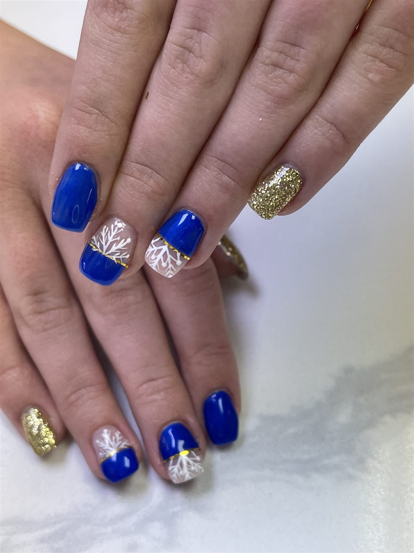 Royal blue nails with white botanical line art and gold glitter accents
